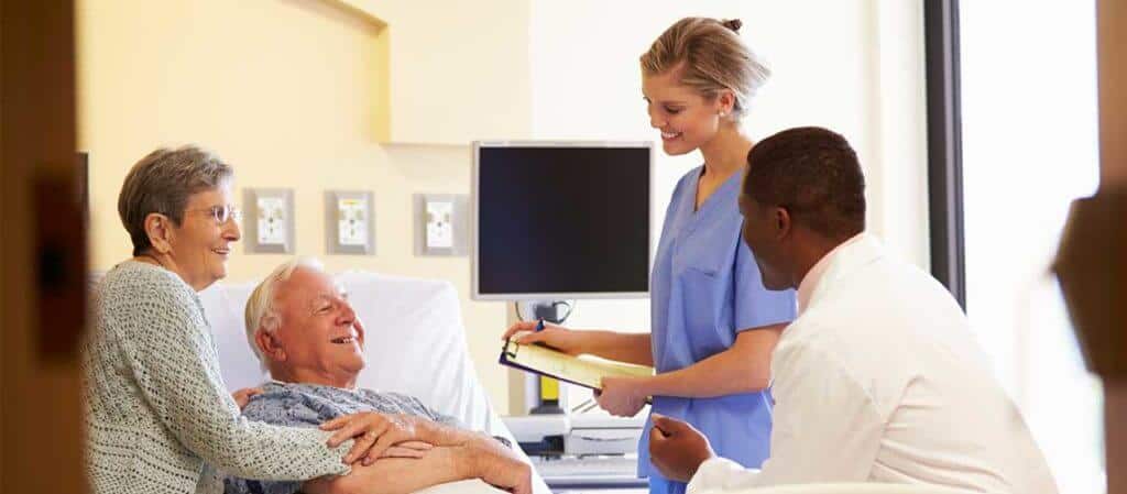 A patient lying in a hospital bed with his wife beside him speaking with his doctor and nurse