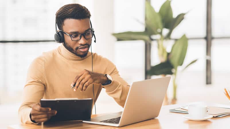 Young black man in orange sweater at his work station