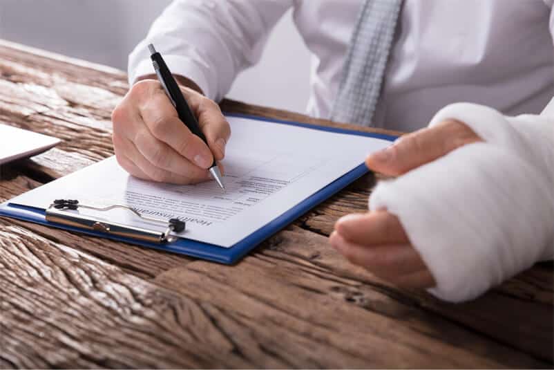 Man in white shirt with bandaged left hand writing out disability claim